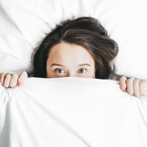 Girl with sheets pulled up to cover her lower face